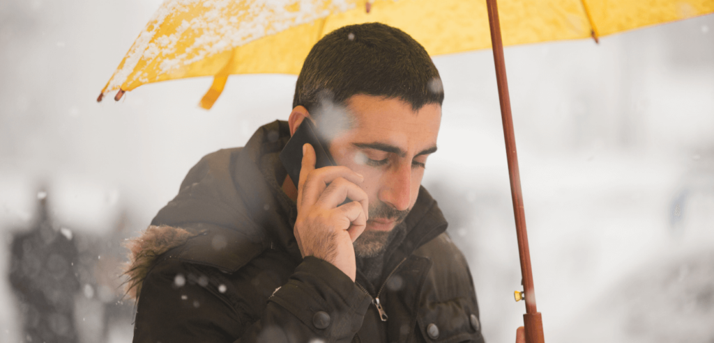 a man in the snow on the phone holding a yellow umbrella, he looks contemplative