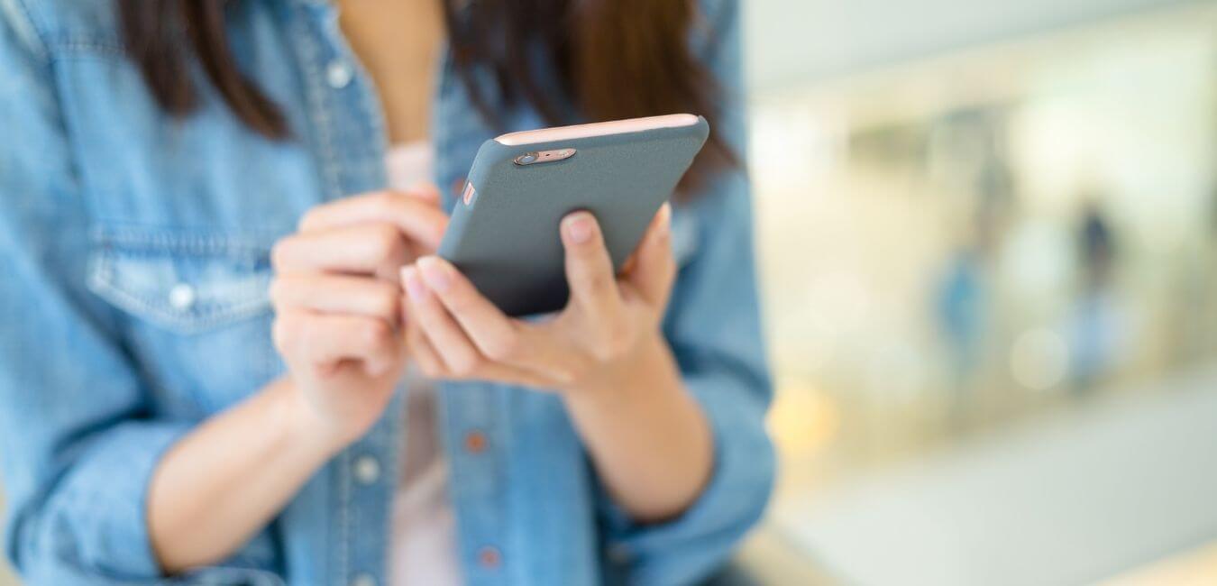 A woman with long brown hair and wearing a denim jacket typing on her mobile phone