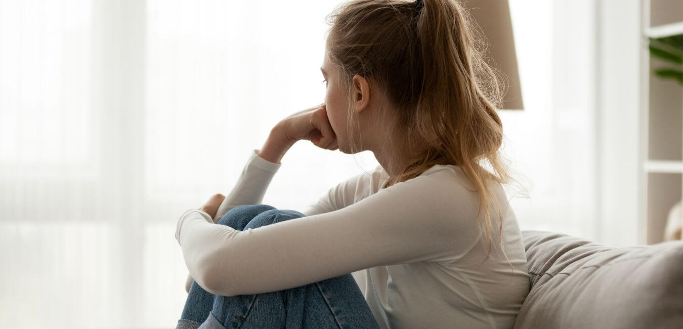Young woman sitting looking out the window looking sad and worried