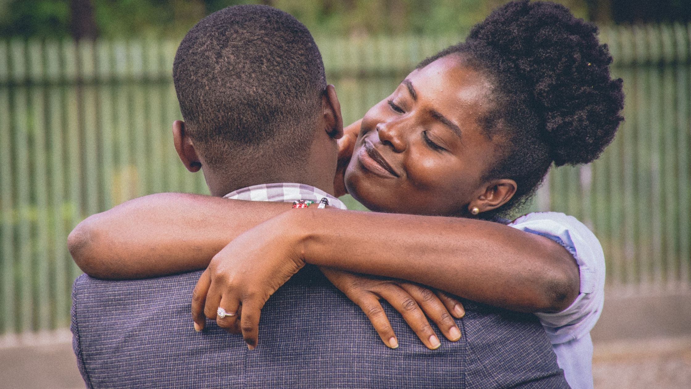 An african american couple embrace. His head is to the camera and her face is happy looking at him