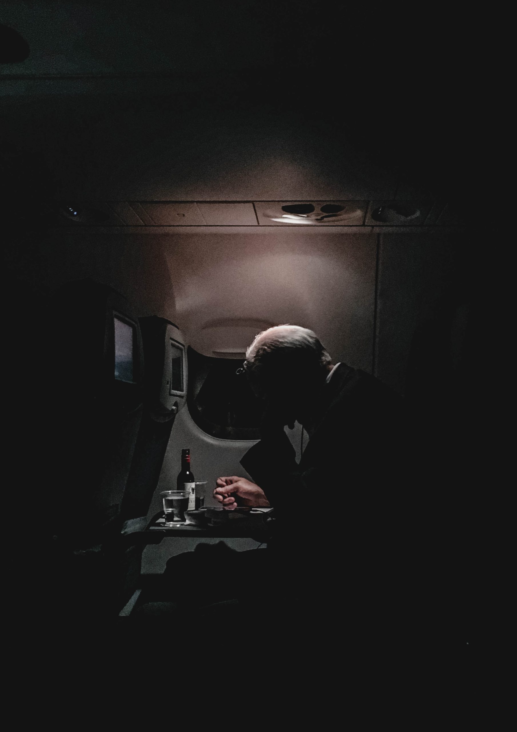 A man is on an airplane with alcohol on his tray table. He is looking down in anguish