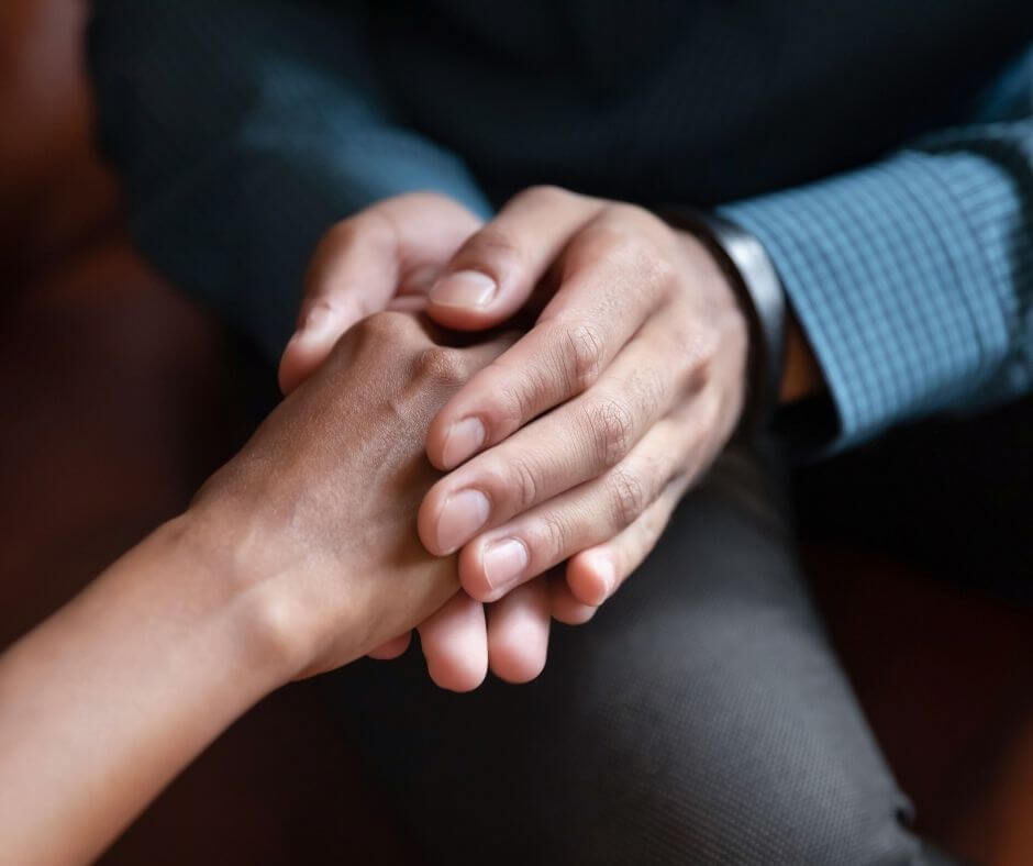 Two people - one with darker skin, the other with lighter brown skin - grasp each other's hands in a show of support