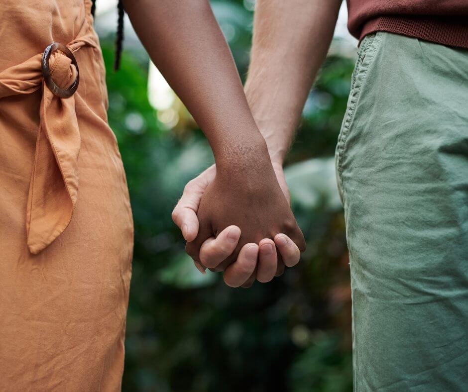 A couple with darker skin tones holds hands with their fingers interlaced