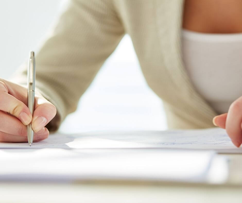 A woman presses her pen to a piece of paper to begin writing a letter.