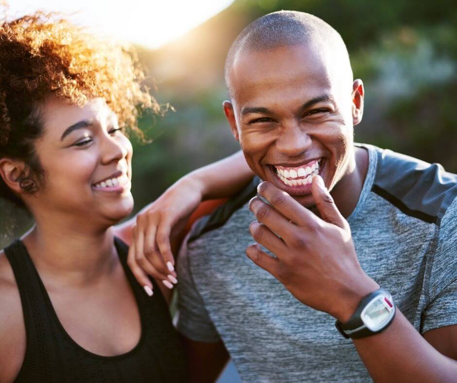 A Black couple laughing together. They both seem to be wearing active wear and enjoying some time outdoors.