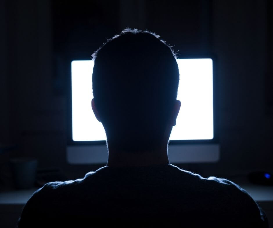 A man stares at a computer screen in the dark.