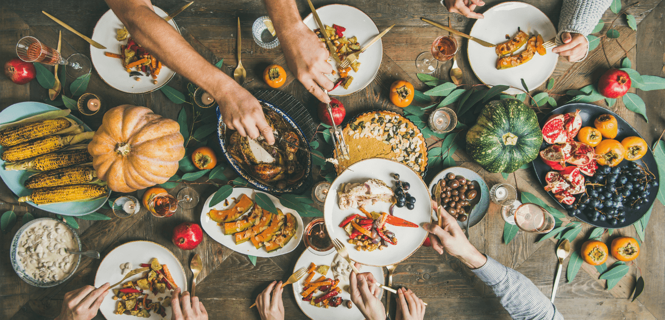 A thanksgiving table, covered in dishes and food. One person holds out a plate while another portions something on for them.