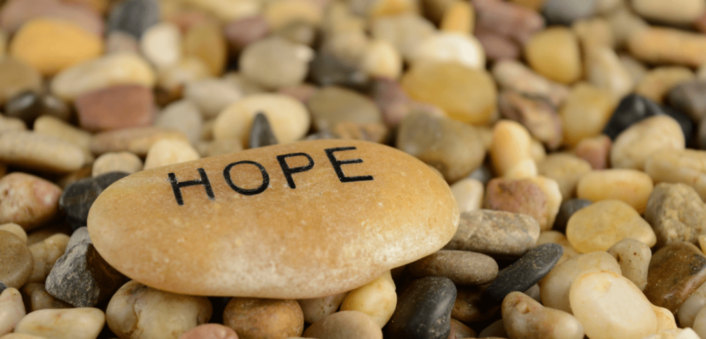 A pile of small rocks with one larger on top that says, "Hope"