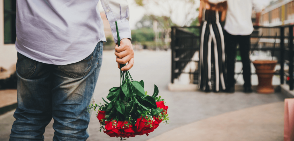 Man wearing blue long sleeve holding flowers for his girlfriend but he saw his lover with someone else