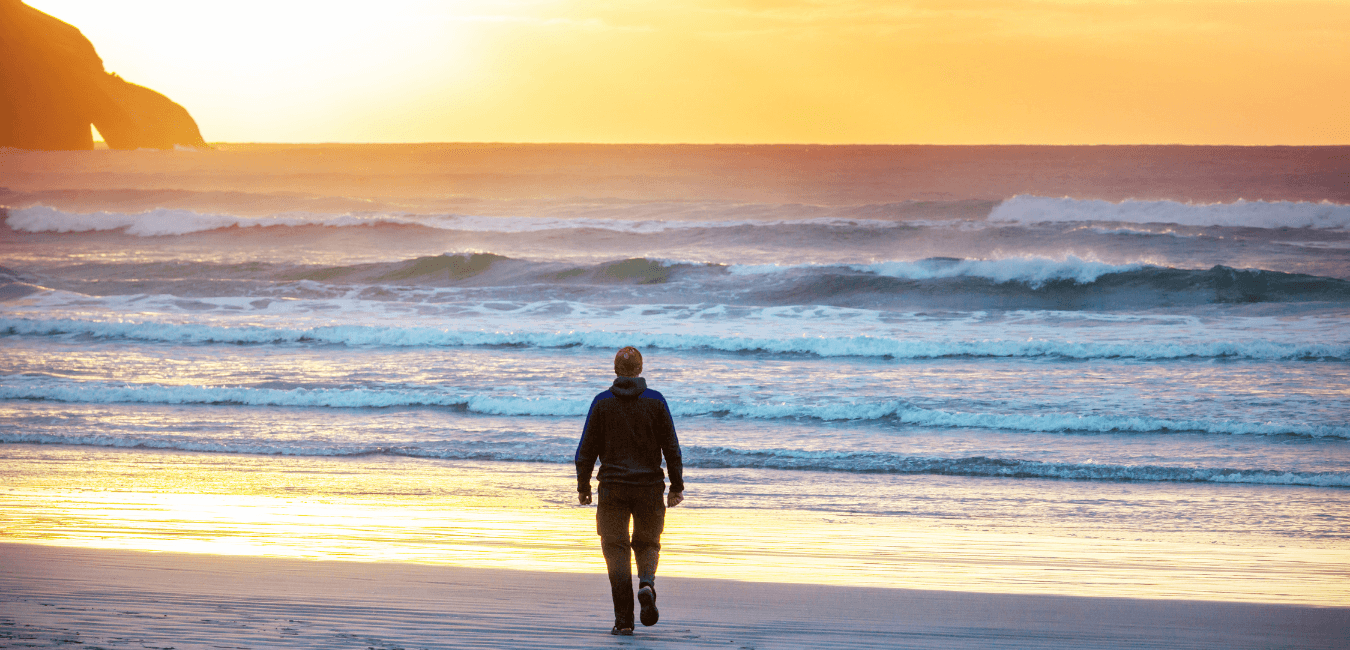 Man wearing a jacket and a beaning walking towards the sea at sunset