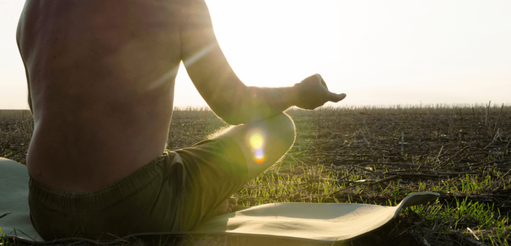 Shirtless man meditating during sunrise sitting on yoga mat