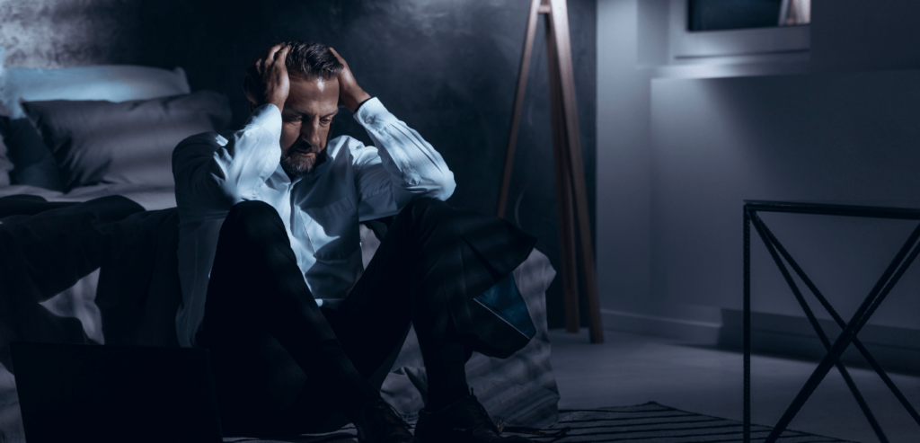 Man wearing office attire on his bed looking problematic in a dark room