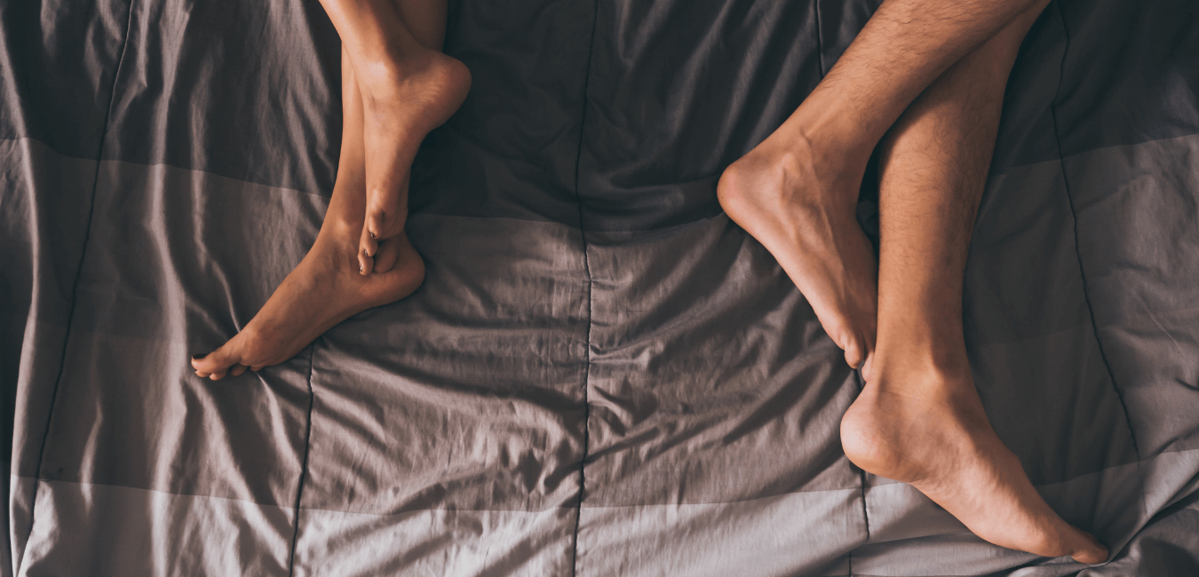 Close up photo of the legs of a couple on the bed