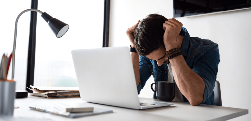 Man sitting on his desk with his hand on his head looking down