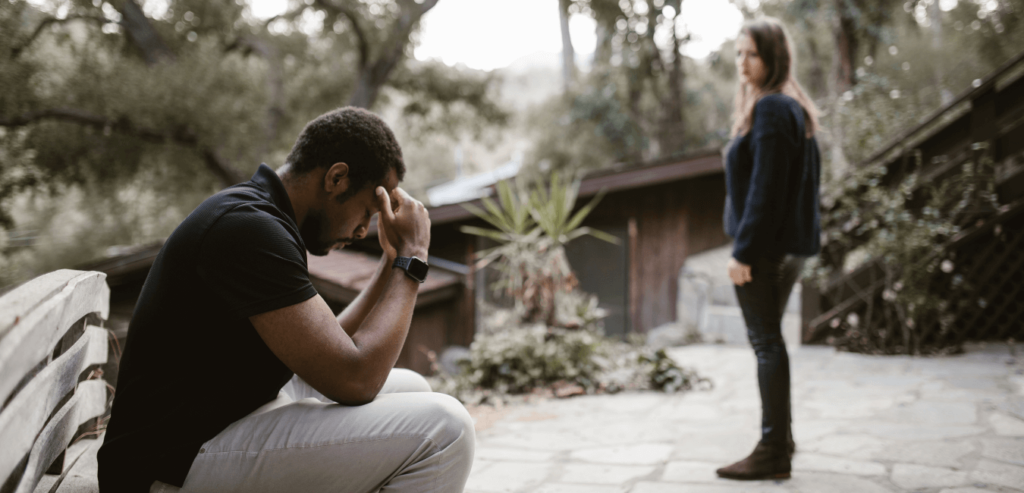 Couple after a fight, man sitting on the side while woman standing from far