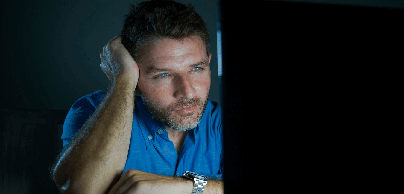 Man looking at computer monitor screen sitting at his desk in a dark room