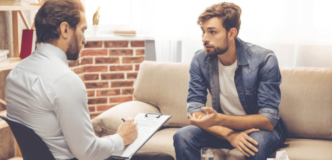Man sitting on couch talking to therapist while he's writing notes in a room