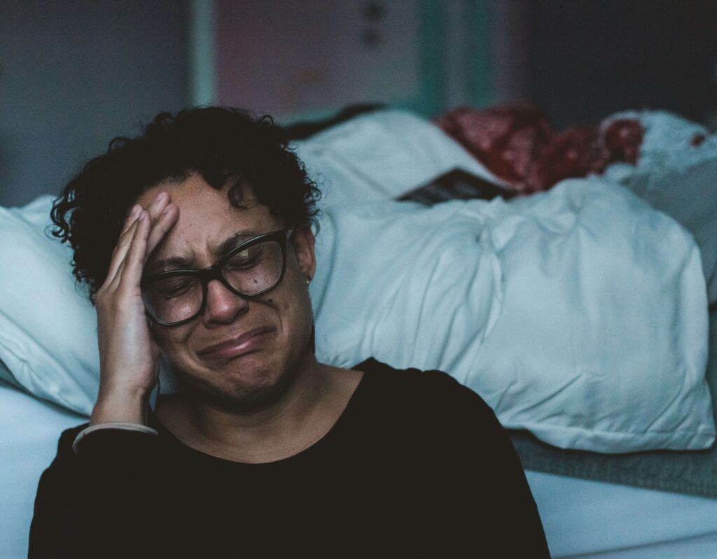 Depressed man sitting on floor crying behind his bed