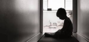 Black and white photo of a young boy sitting on a hallway at home looking sad