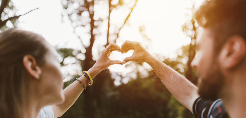 Happy couple making heart shape sign with hands at sunrise
