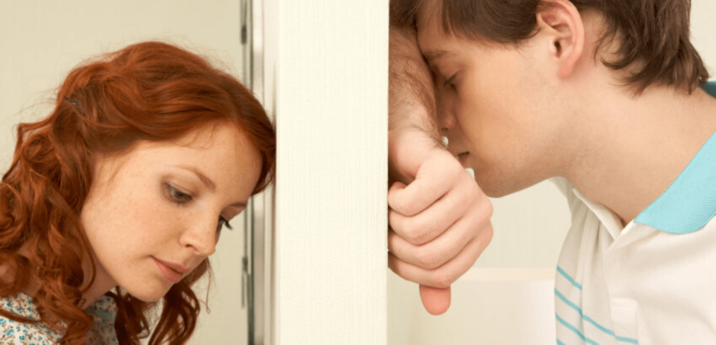 Young married couple leaning on opposite sides of the wall looking like going through a problem