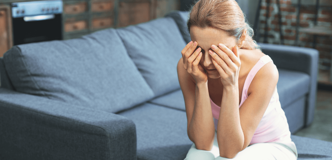 Woman sitting on couch at home looking depressed with hand on her eyes