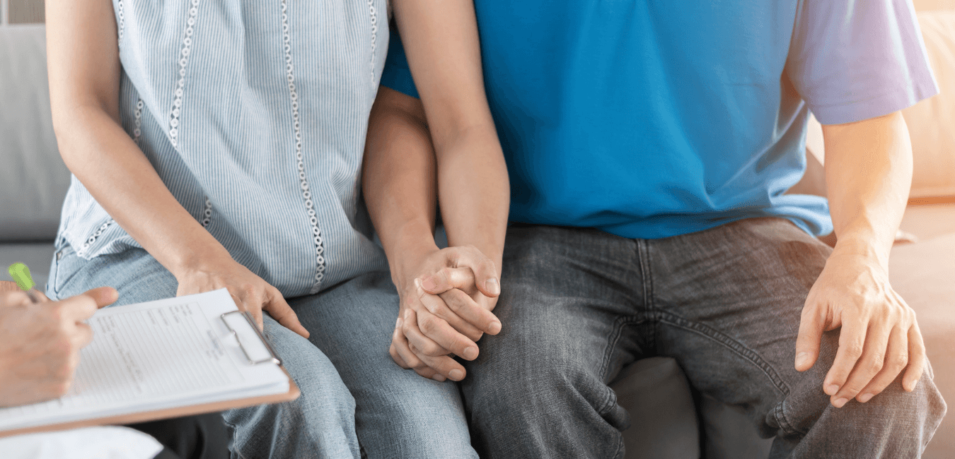 Couple sitting on couch holding hands talking to a therapist writing notes