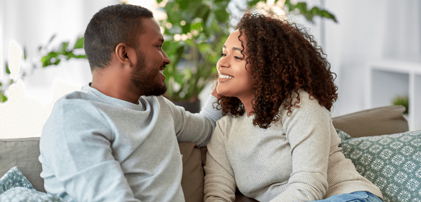 African couple sitting on sofa at home smiling having conversation