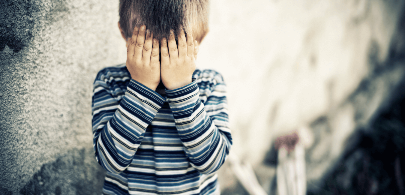 Young boy standing behind wall looking unhappy crying hiding his face