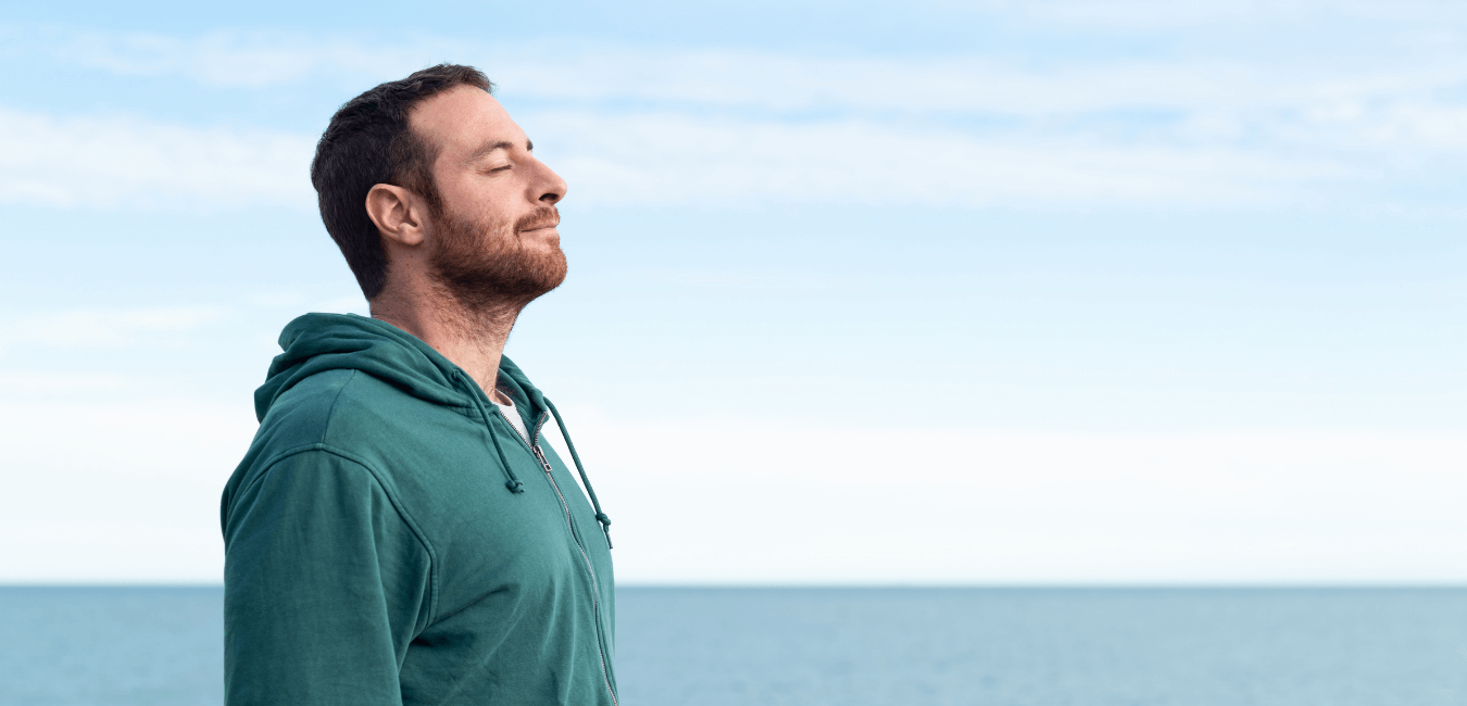 Man breathing deeply fresh air standing outdoors in front of the ocean