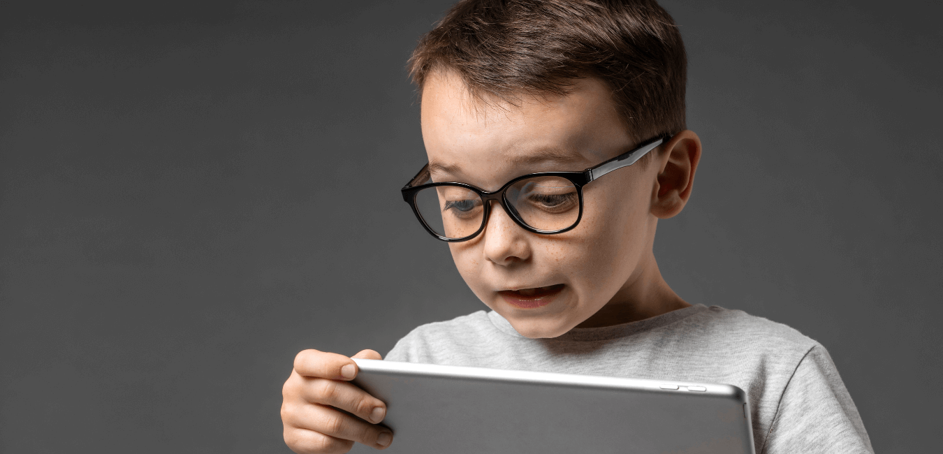 Kid wearing glasses holding and using tablet looking astonished