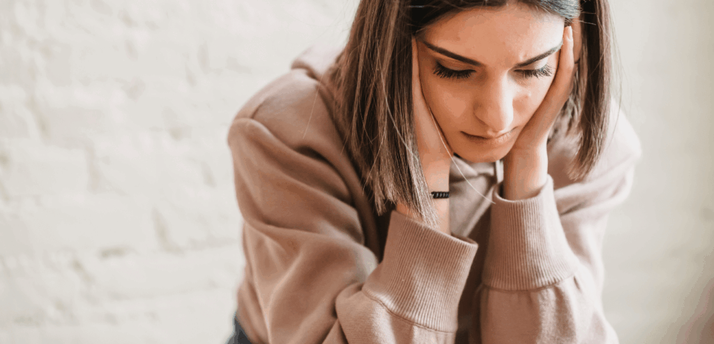 Young woman sitting in the corner with her hand on her face, quiet, and looking sad.