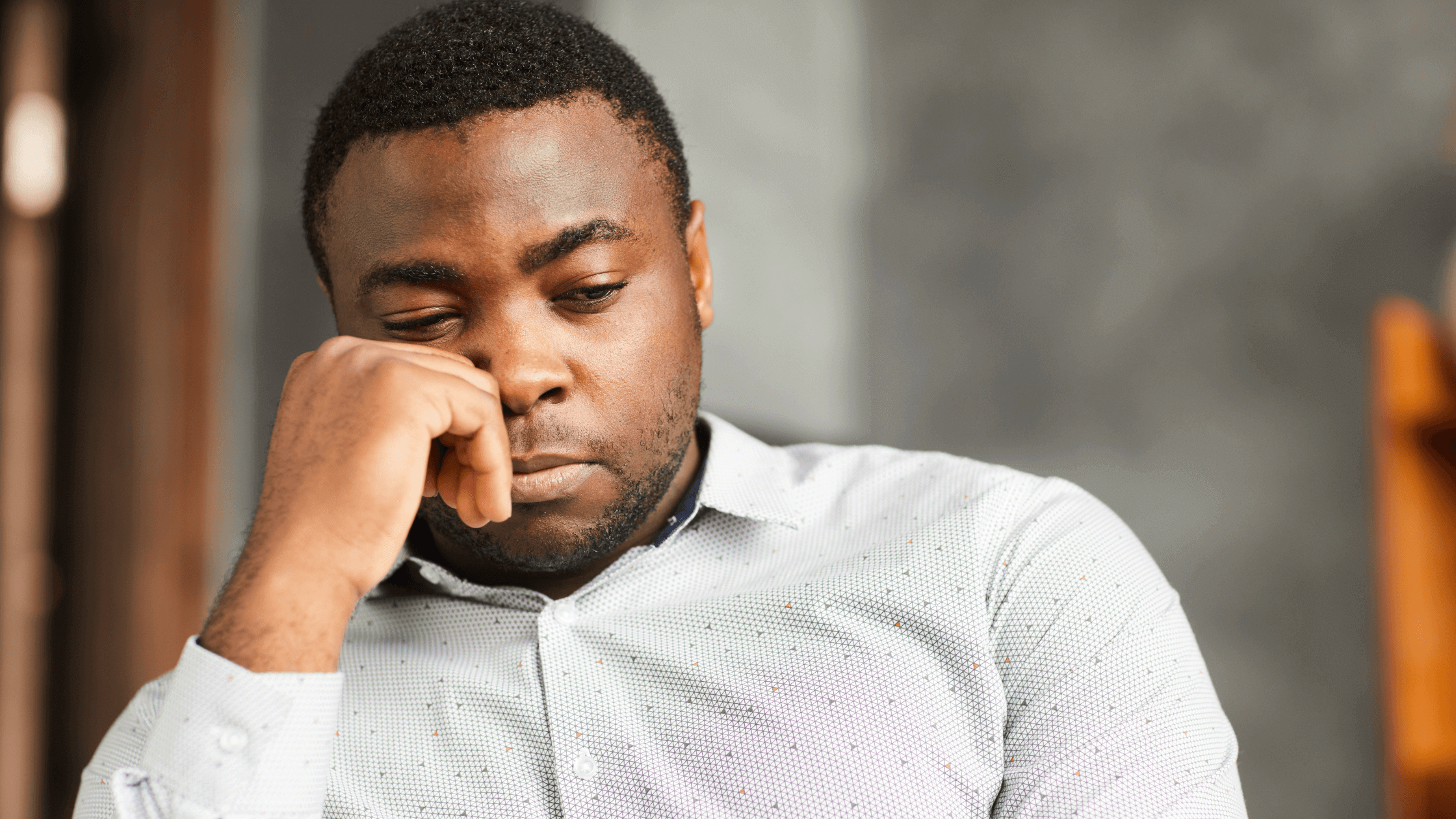 A man of color sits alone in the corner, deep in thought, his hand resting on his face.