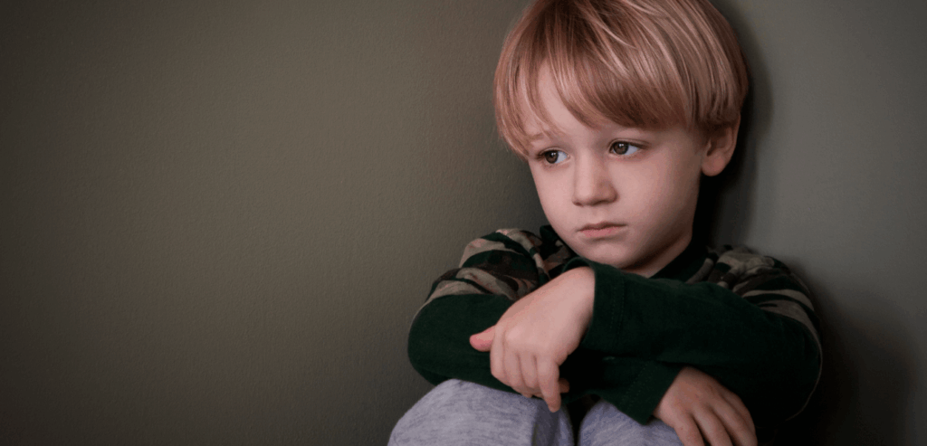 Child sitting quietly, and alone in the corner in house looking sad