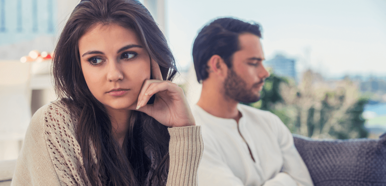 Married couple sits silently on the couch at home, their tension lingering after an argument