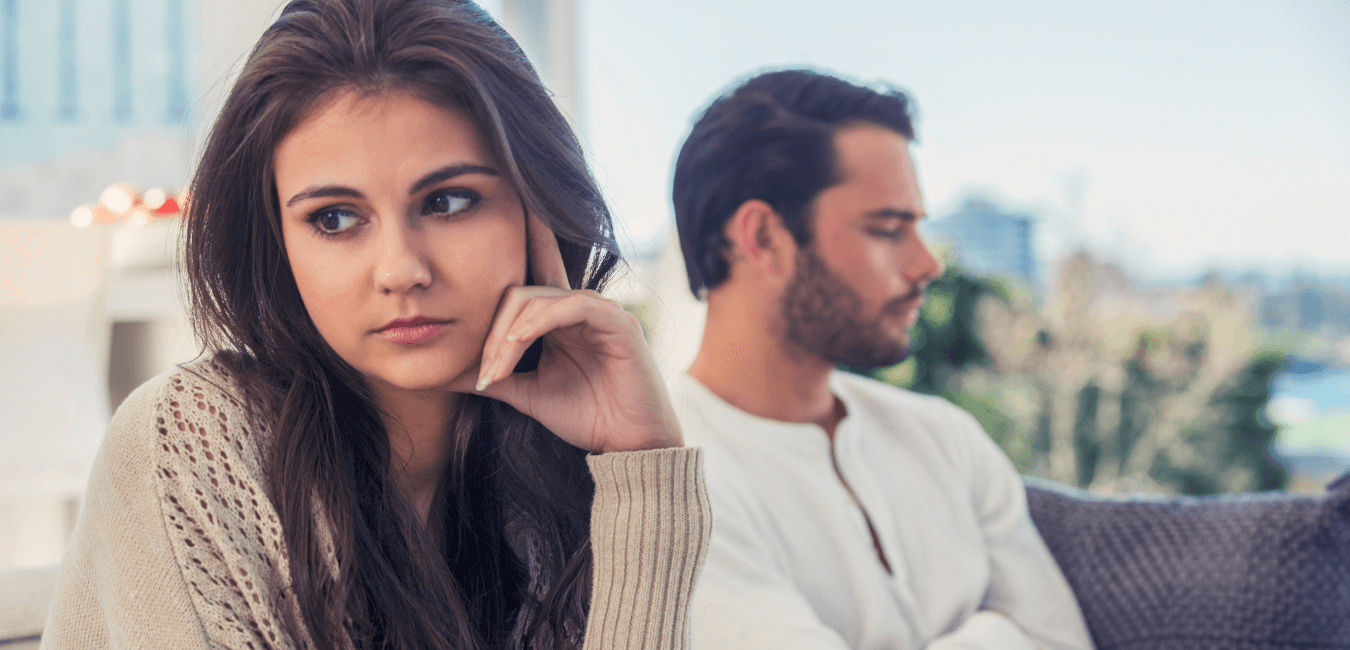 Young couple sits quietly on the couch, not talking or looking at each other, as if something is wrong.