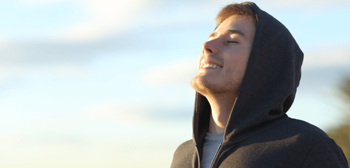 Man in a hoodie smiling outside, taking a deep breath of fresh air.