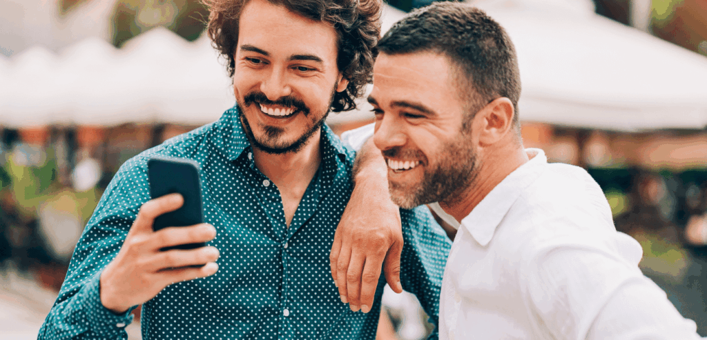 Two men enjoying a conversation outside, both smiling and focused on a smartphone.
