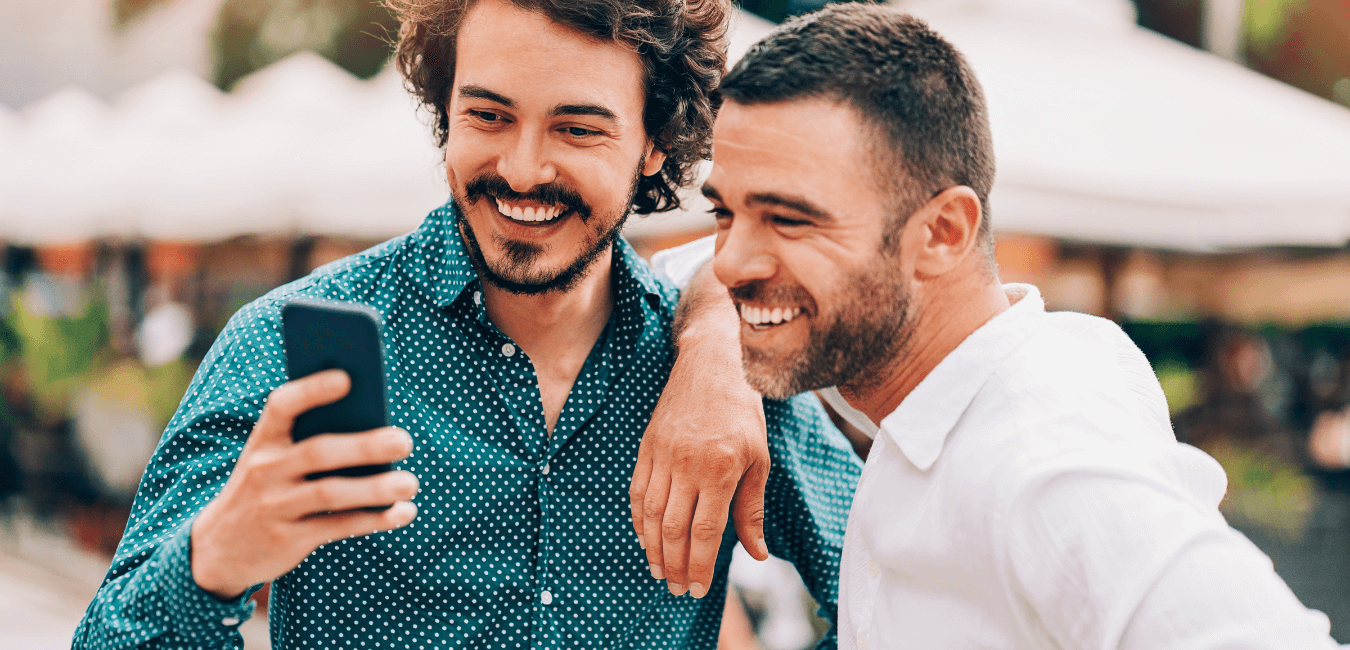 Two men enjoying a conversation outside, both smiling and focused on a smartphone.