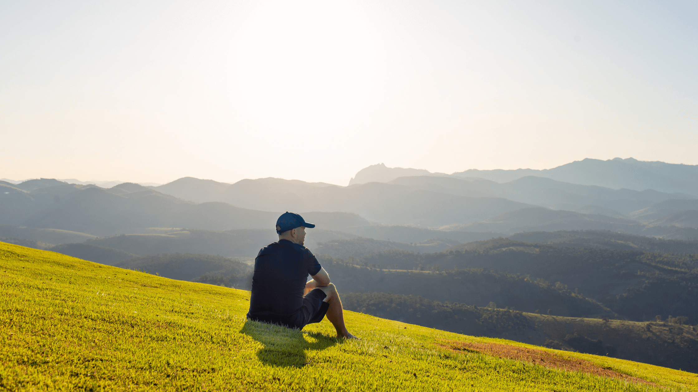 Man wearing a cap enjoys the quiet outdoors, sitting in a sunny field of grass