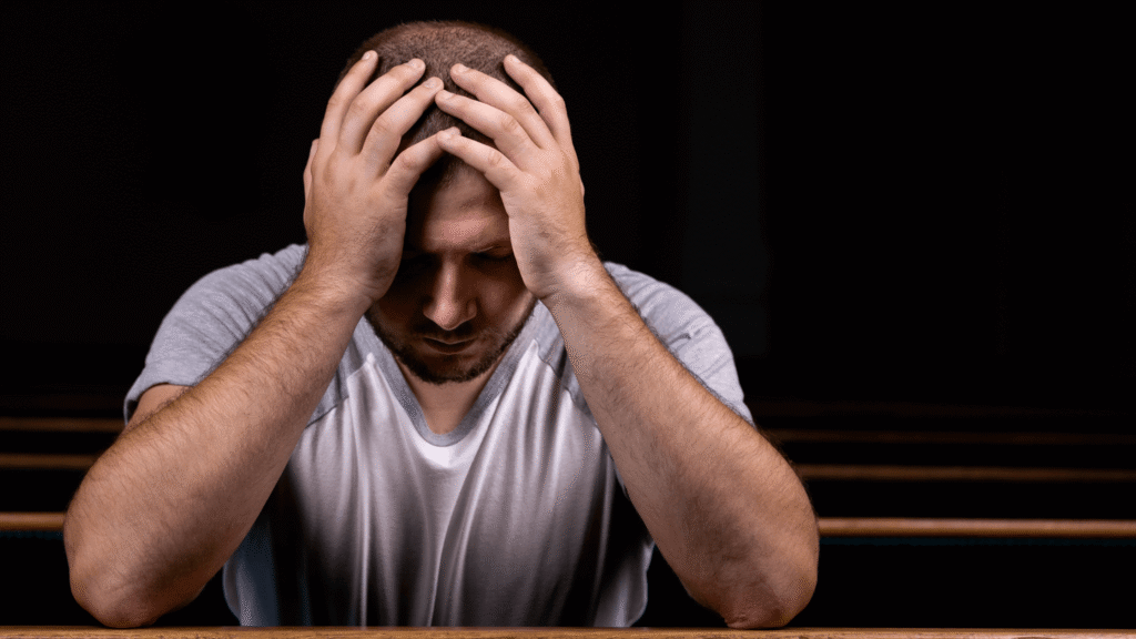 Man sitting quietly, hand on head, looking down