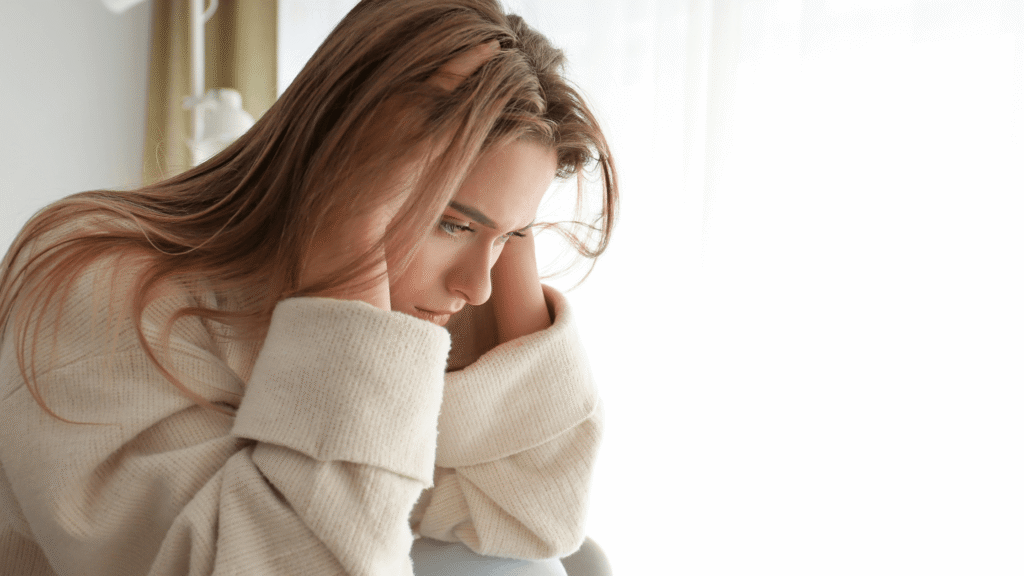 Woman sitting quietly in corner of room, sweater on, deep in though