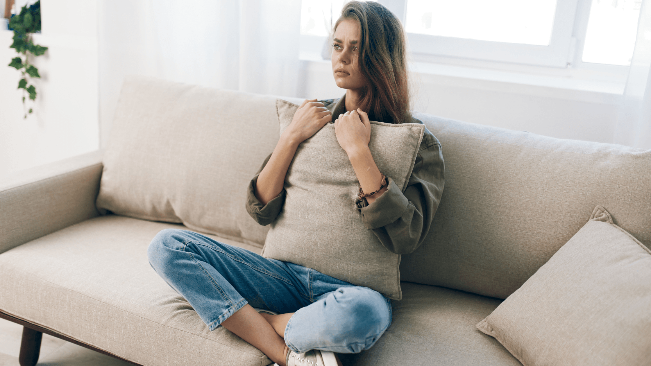 Woman sitting on couch at home, looking sad and holding a pillow