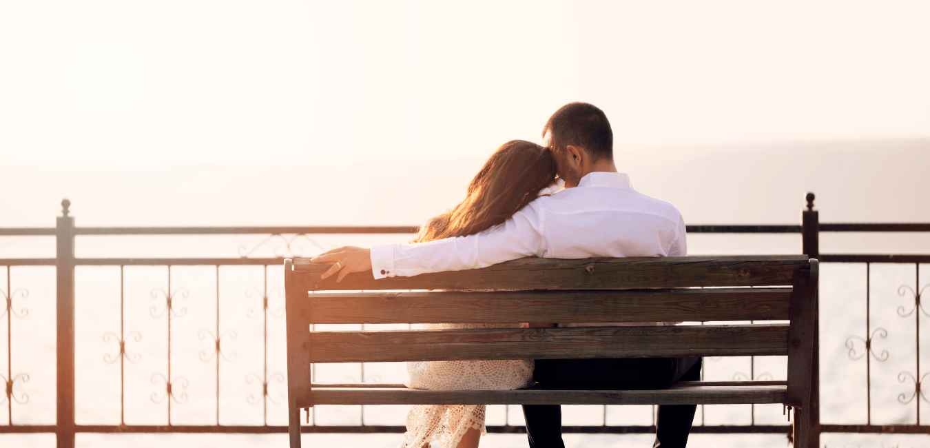 Young married couple sitting affectionately on the beach, watching the sunset.