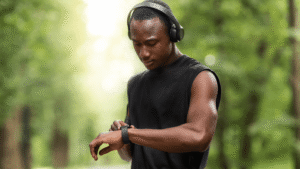 Man of color outdoors in headphones, looking at his smartwatch before running.