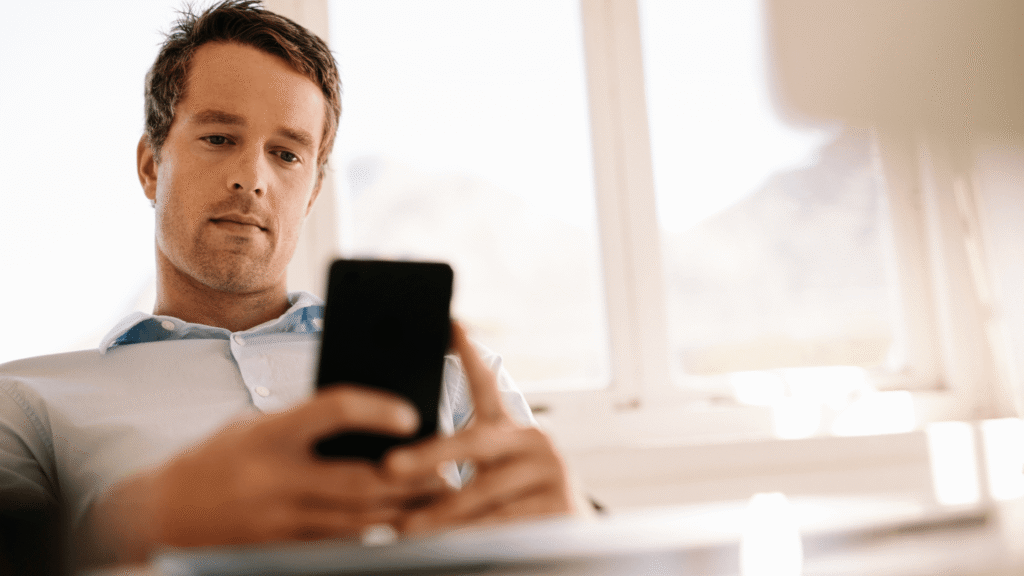 Man sitting and using his phone, with a serious expression while engaged in conversation.