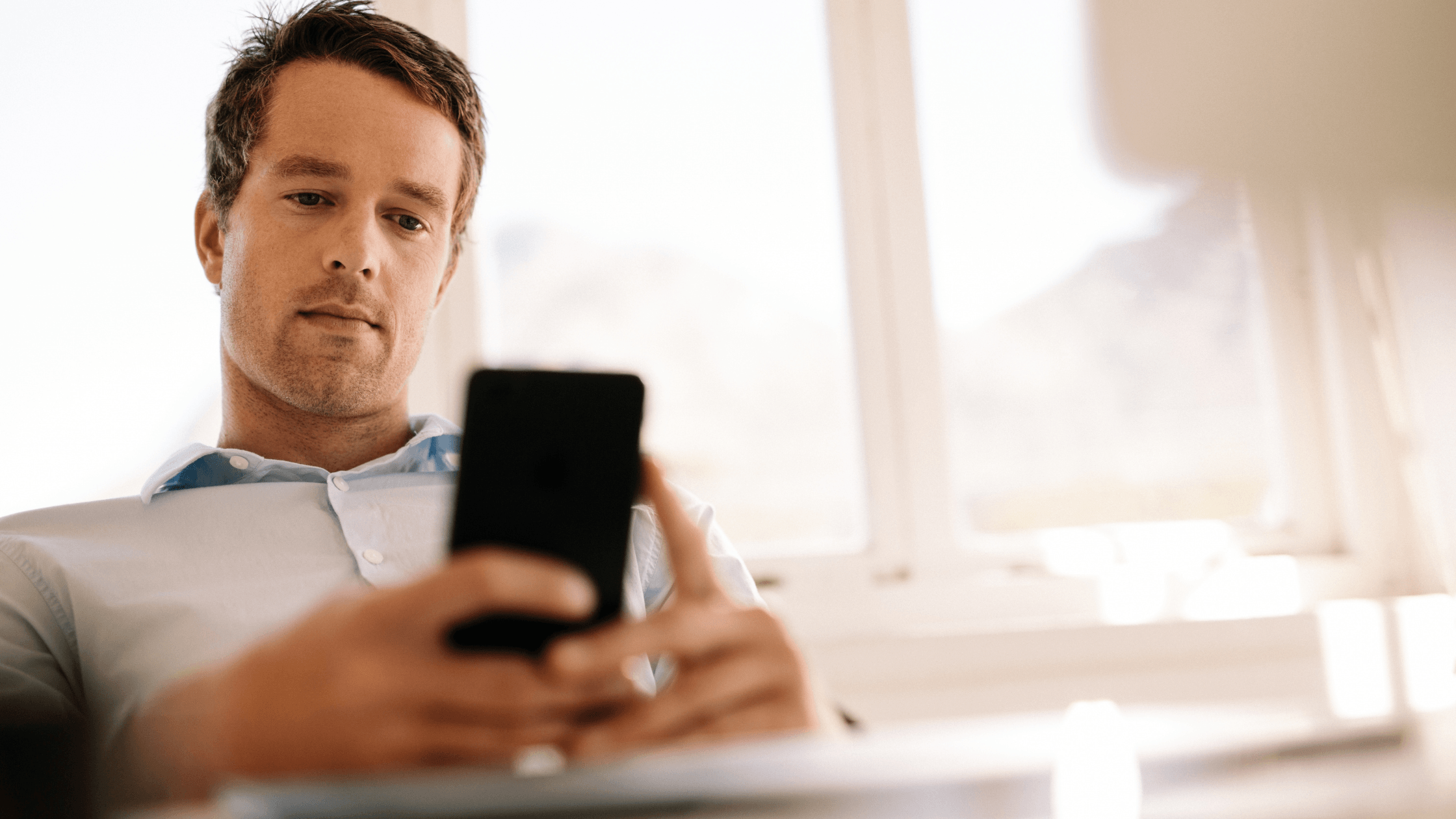 Man sitting and using his phone, with a serious expression while engaged in conversation.