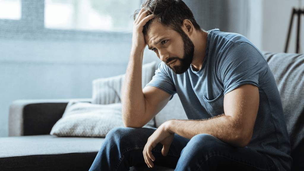 Man sitting in living room with his hand on his head, appearing deep in thought.