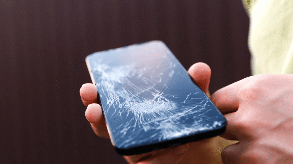 Close-up of a man holding a mobile phone with a completely broken screen.