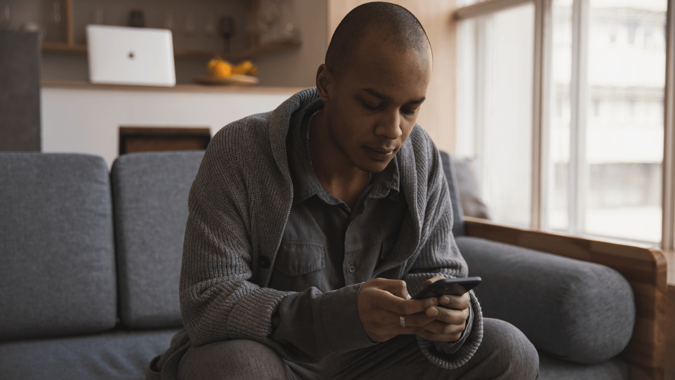 Man of color sitting on a sofa at home, looking serious while using his phone.
